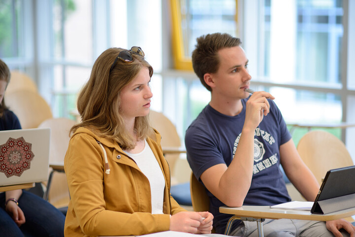 Zwei Studierende sitzen nebeneinander im Seminarraum und schauen aufmerksam nach vorne.