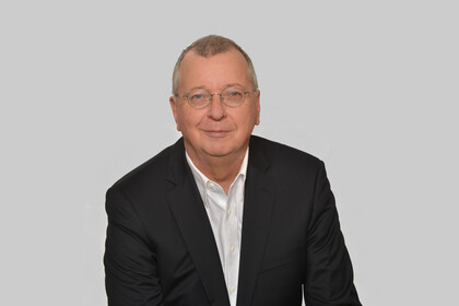 Portrait von Prof. Dr. Weber. Er trägt einen Anzug und sitzt vor einer weißen Wand.