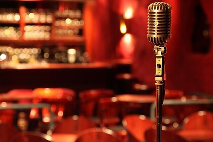 Im Zentrum ist ein Mikrofon abgebildet und im Hintergrund sieht man verschwommen eine Bar.