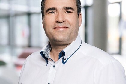 Porträt von Oliver Klinck in der Reihe "Alumuns of the Month". Klinck trägt ein weißes langärmliges Hemd und die Haare kurz. Er lächelt freundlich in die Kamera. Link: Insta Alumnus of the month