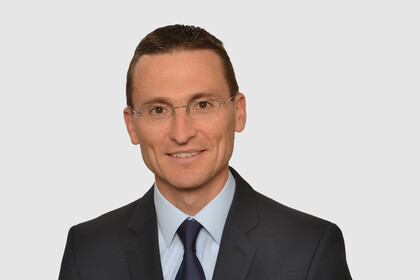 Prof. Brauer hat kurze Haare und eine Brille. Er trägt ein dunkles Jacket, ein hellblaues Hemd und eine dunkelblaue Krawatte.