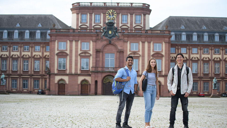 Studierende auf dem Ehrenhof Drei Studierende auf dem Ehrenhof gucken in Richtung Kamera. Im Hintergrund der Mittelbau des Schlosses.