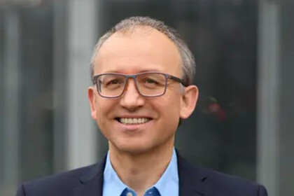 Portrait von Thomas Gschwend. Er trägt ein hellblaues Hemd sowie einen dunkelblauen Blazer unf steht lächelnd vor einem Fenster.