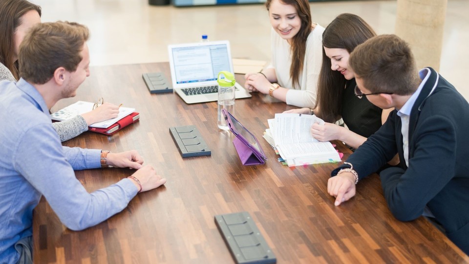 Studierende mit Lernmaterialien sitzen um Tisch