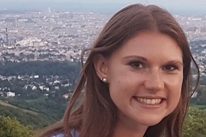 Victoria Meil trägt einen hellblauen Pullover und hat lange braune Haare. Sie steht auf einer Erhöhung, im Hintergrund sieht man das Panorama einer großen Stadt.