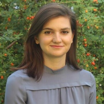 Dieses Bild zeigt Kristina Petrova, eine Frau mit schulterlangen braunen Haaren und grauer Bluse