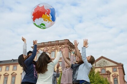 Eine Gruppe von Studierenden steht im Ehrenhof im Kreis. Sie werfen gemeinsam einen großen Wasserball in die Luft. Der Wasserball ist transparent und stellt ein Modell der Erde dar. Die Kontinente sind in unterschiedlichen Farben markiert. Im Hintergrund ist einen Teil des Barockschlosses zu sehen. Link: Instagram-Post ENGANGE-EU University Campus
