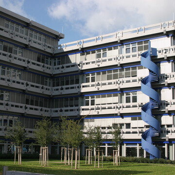Gebäude der Fakultät für Sozial­wissenschaften mit blauer Wendeltreppe. Davor eine Wiese mit Bäumen.