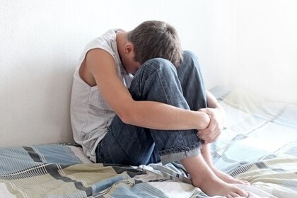 Ein Teenager sitzt auf einem Bett und hält seinen Kopf zwischen den Knien.