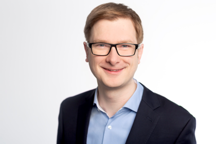 Benjamin Engst trägt einen schwarzen Blazer über hellblauem Hemd. 