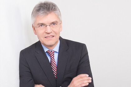 Portrait von Christoph Spengel. Er trägt ein schwarzes Jackett und lehnt an eine weiße Wand.