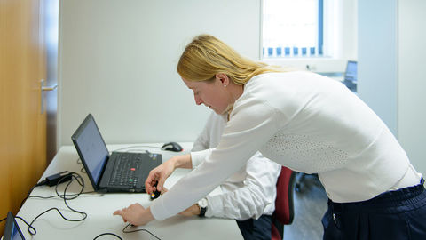Eine Frau legt einer Person, die vor einem Laptop am Tisch sitzt, einen Fingersensor an.