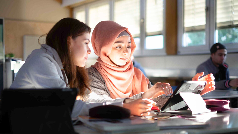 Lehrerausbildung Zwei junge Frauen sitzen in einem Seminarraum und interagieren mit einem Tablet