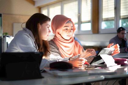 Zwei junge Frauen sitzen in einem Seminarraum und interagieren mit einem Tablet