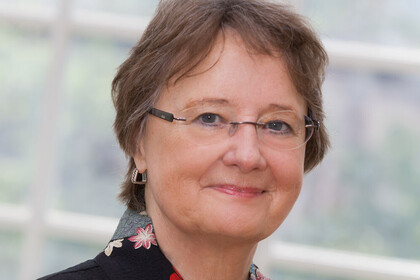 Portrait von Rosemarie Tracy. Sie trägt ein geblümtes Oberteil und steht vor einer Fensterfront.