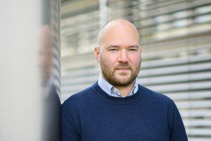 Porträt von Prof. Traunmüller. Er trägt einen dunklen Pullover und lehnt an einer Säule.
