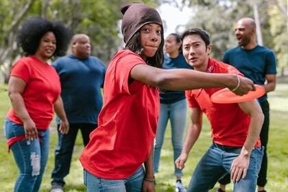 Eine Gruppe mit jeweils roten und dunkelblauen T-Shirts spielt mit einem Frisbee. Unten rechts ist das Logo des IFS- Institut für Sport der Universität Mannheim.