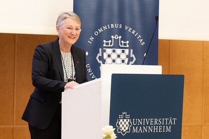 Kanzlerin Barbara Windscheid steht am Rednerinnenpult in der Aula der Universität Mannheim. Sie trägt einen dunklen Hosenanzug und ein weiß-schwarz gemustertes Oberteil sowie eine rahmenlose Brille. Link: Instagram Verabschiedung Kanzlerin
