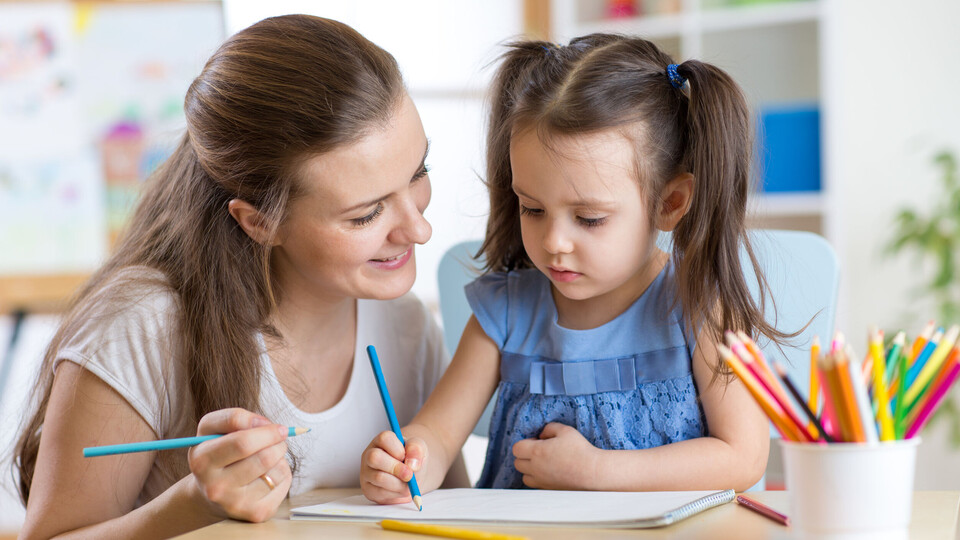 Mother looking how her child daughter drawing a picture