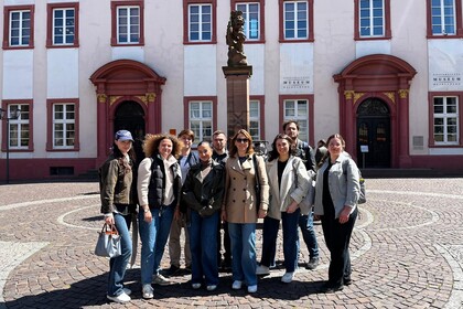 Eine Gruppe von 9 Personen steht vor einem Brunnen auf einem gepflasterten Platz vor einem historischen Gebäude.