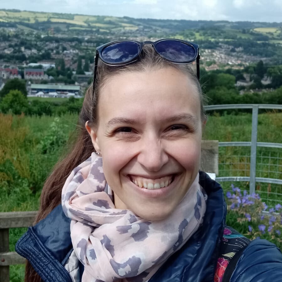 Vera Vogel im Freien. Sie trägt eine Sonnenbrille auf dem Kopf und einen gemusterten Schal, dazu eine Jeansjacke.