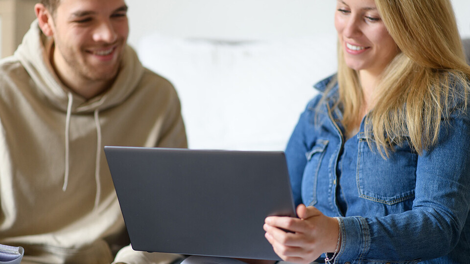 Eine junge Frau zeigt einem jungen Mann etwas auf dem Laptop.