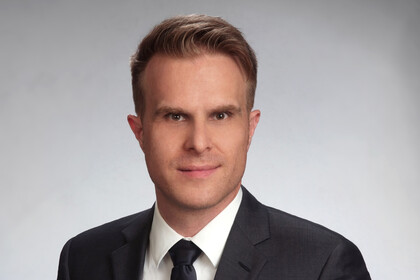 Portrait von Florian Stahl. Er trägt ein weißes Hemd, eine schwarze Krawatte und ein dunkelgraues Sakko.