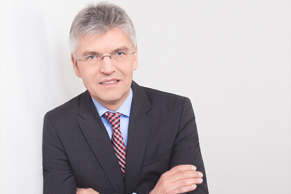 Portrait von Christoph Spengel. Er trägt ein hellblaues Hemd, eine rote Krawatte sowie einen schwarzen Blazer und hat seine Arme vor der Brust verschränkt.