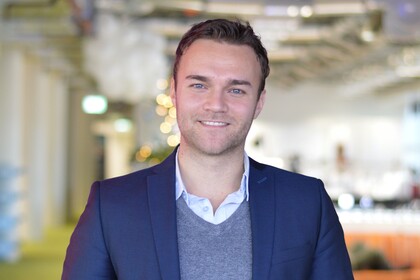 Kevin Bauer hat Kurze Haare und trägt ein Hemd, einen Pullover und ein Jacket.