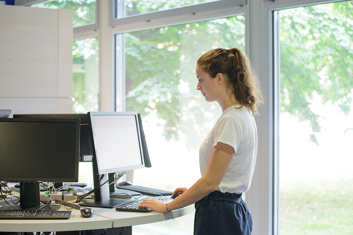 Eine Studentin steht am Computer-Stehpult in der Bibliothek.