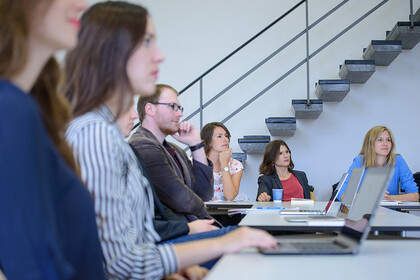 Junge Frauen und Männer sitzen mit ihren Laptops in einem Seminarraum.