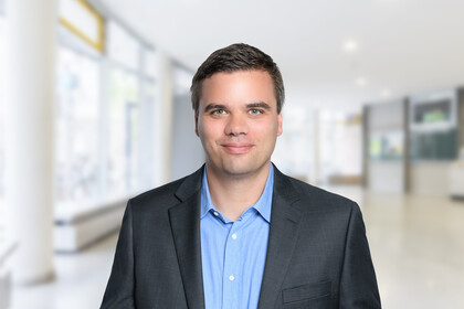 Christoph Rothe trägt ein blaues Hemd und einen grauen Sakko, im Hintergrund ist ein Büro zu erahnen.