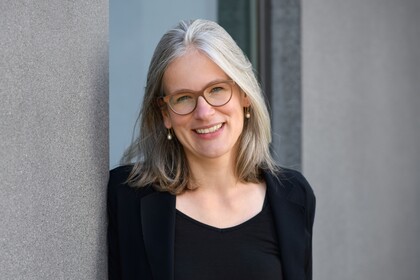 Gesundheitspsychologin Prof. Dr. Jutta Mata lehnt an eine Betonwand und lächelt. Sie trägt einen schwarzen Blazer und ein schwarzes T-Shirt.