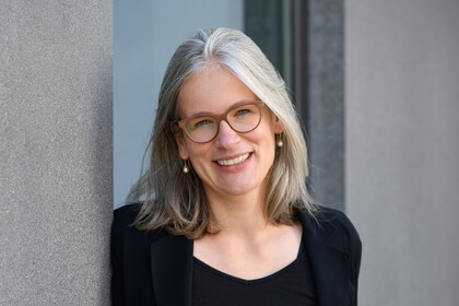 Gesundheitspsychologin Prof. Dr. Jutta Mata lehnt an eine Betonwand und lächelt. Sie trägt einen schwarzen Blazer und ein schwarzes T-Shirt.