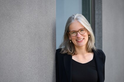 Gesundheitspsychologin Prof. Dr. Jutta Mata lehnt an eine Betonwand und lächelt. Sie trägt einen schwarzen Blazer und ein schwarzes T-Shirt.