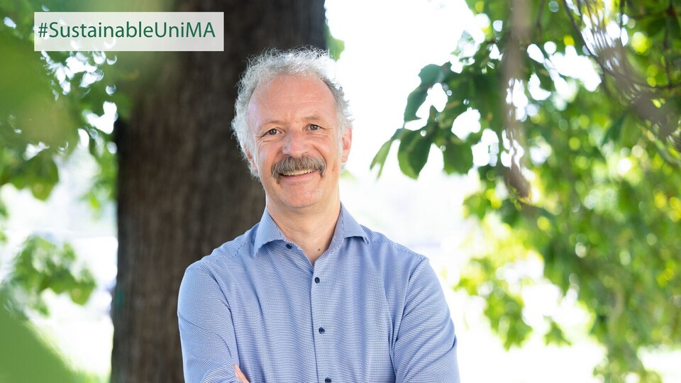Prof. Dr. Moritz Fleischmann. Er lächelt, sein Hemd ist hellblau gestreift und er hat einen Schnurrbart.