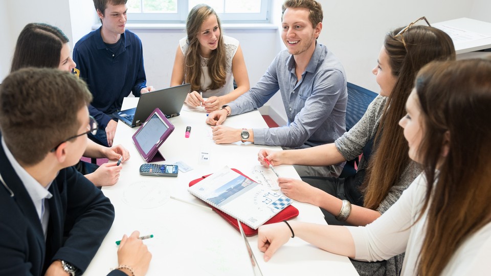 Studierende mit Laptops sitzen um einen Tisch