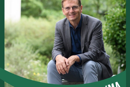 Porträt von Prof. Dr. Oliver Dickhäuser für die Serie "Green Uni Ma". Er sitzt auf einem Stein in einem begrünten Innenhof. Er trägt Jeans, ein dunkelblaues Hemd und ein graues Sakko. Seine Haare sind kurz und hellbraun. Er trägt eine Brille mit dünnem Gestell und lächelt in die Kamera. Link: Instagram-Post Green Uni Ma Porträt