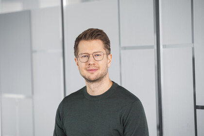 Alexander Bellin hat kurze braune Haare und trägt ein dunkelgraues Langarmshirt und eine Brille