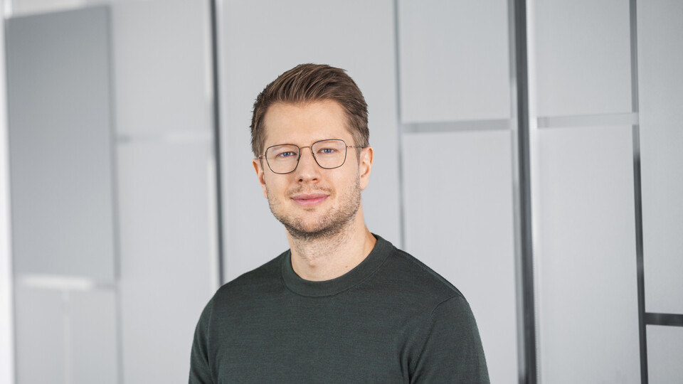 Alexander Bellin hat kurze braune Haare und trägt ein dunkelgraues Langarmshirt und eine Brille