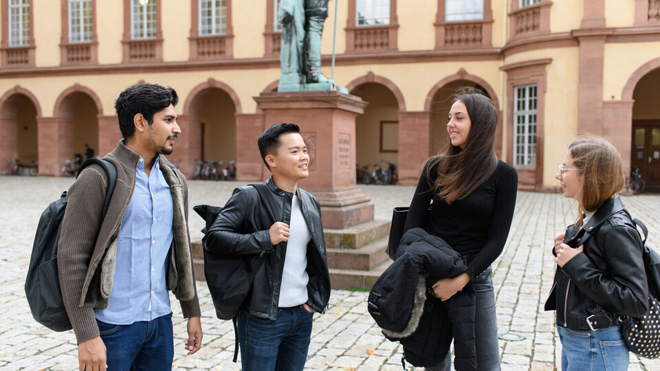 Eine Gruppe Studierende steht im Ehrenhof des Schlosses. Sie unterhalten sich. Im Hintergrund sieht man Teile einer Statue.