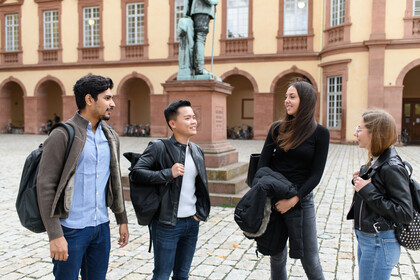 Eine Gruppe Studierende steht im Ehrenhof des Schlosses. Sie unterhalten sich. Im Hintergrund sieht man Teile einer Statue.