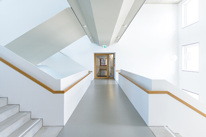 Innenaufnahme des weißen Treppenhauses von B6 mit Holzelementen am Treppengeländer und Türrahmen. 