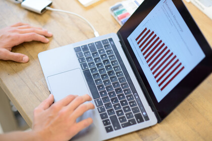 Hande schreiben an einem Laptop. Auf dem Monitor ist ein Diagramm.