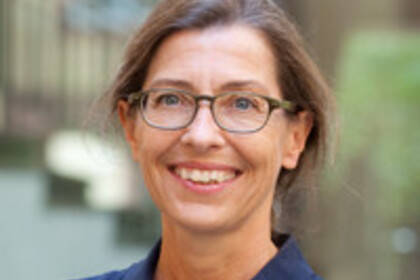 Portrait von Julia Angster. Sie trägt eine dunkelblaue Bluse und steht lächelnd vor einem Gebäude.