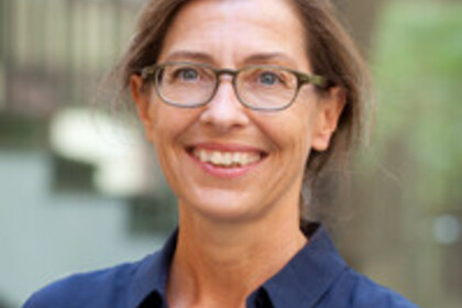 Portrait von Julia Angster. Sie trägt eine dunkelblaue Bluse und steht lächelnd vor einem Gebäude.