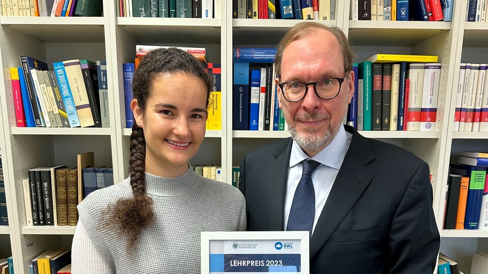 Zwei Personen stehen vor einem Bücherregal und halten eine Urkunde zwischen sich