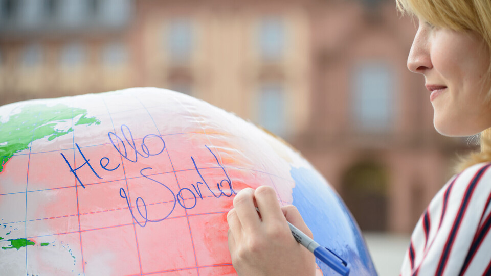 Frau mit blonden Haaren schreibt mit einem Stift einem Luftballon, der aussieht wie eine Weltkugel.