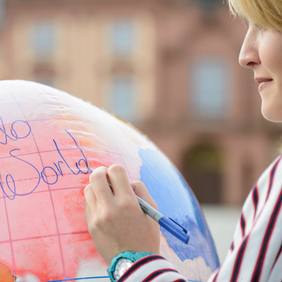 Frau mit blonden Haaren schreibt mit einem Stift einem Luftballon, der aussieht wie eine Weltkugel.