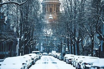 Blick auf den Wasserturm. Es ist eine verschneite Straße mit parkenden Autos zu sehen. Daneben stehen mit Schnee bedeckte Bäume